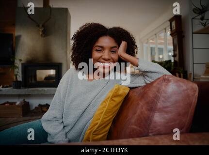Portrait of smiling beautiful young woman relaxing on sofa at home during covid-19 lockdown Stock Photo