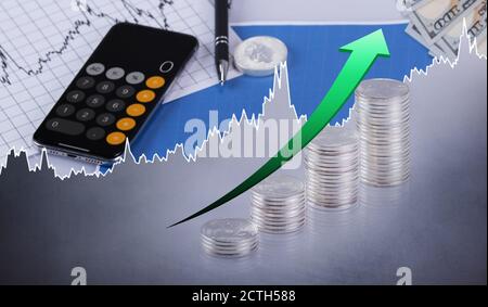 Rising Silver Prices Concept. Stacks of Silver coins with green arrow pointing up with calculator and pen. Stock Photo