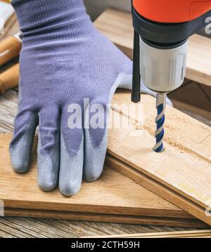 Man working with a hand drilling tool on the work bench. Carpenter gloved hand closeup. Stock Photo