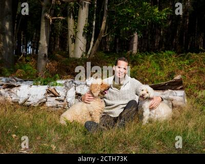 Man sat with dogs in forest, Thetford Forest, Norfolk, UK Stock Photo