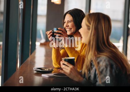 Two women having coffee and smiling. Happy female friends having a great time together in a cafe. Stock Photo