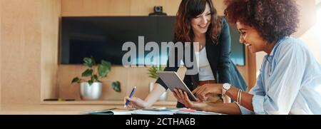 Shot of two businesswoman working together on digital tablet. Creative female executives meeting in an office using tablet pc and smiling. Stock Photo
