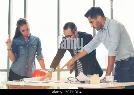 Team of multiethnic architects working on construction plans in meeting room. Engineers discussing on project in office. Mature businessman and woman Stock Photo