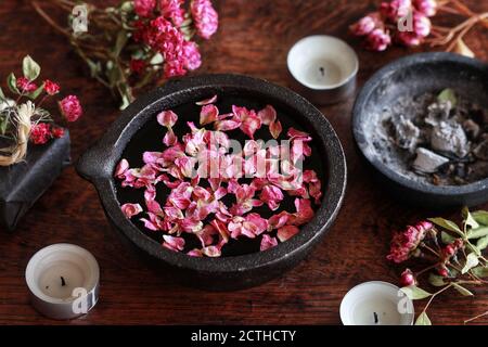 Rose petal infused water on esoteric wiccan witch altar. Pink rose petals floating on water in black cast iron mortar dish Stock Photo