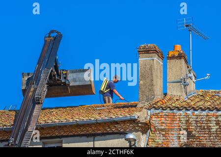 Worked spraying moss on pantile roof - Le Dorat, Haute-Vienne (87), France. Stock Photo