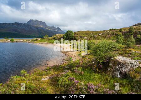 Sandy beach on Loch Maree with rugged crag of Slioch in distance – Loch Maree, Wester Ross, Highland Region, Scotland, UK Stock Photo
