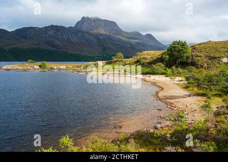 Sandy beach on Loch Maree with rugged crag of Slioch in distance – Loch Maree, Wester Ross, Highland Region, Scotland, UK Stock Photo