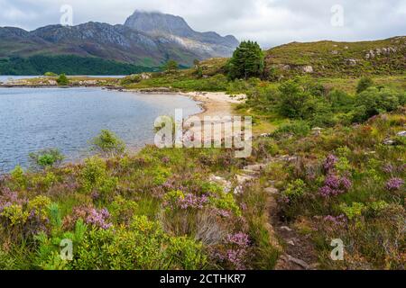 Sandy beach on Loch Maree with rugged crag of Slioch in distance – Loch Maree, Wester Ross, Highland Region, Scotland, UK Stock Photo
