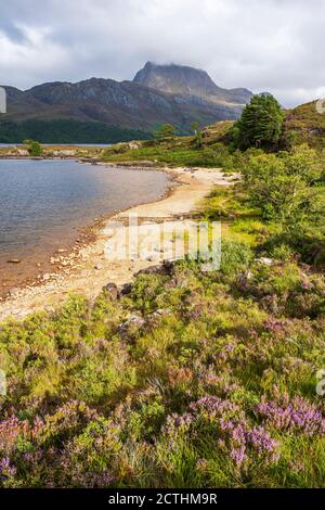 Sandy beach on Loch Maree with rugged crag of Slioch in distance – Loch Maree, Wester Ross, Highland Region, Scotland, UK Stock Photo