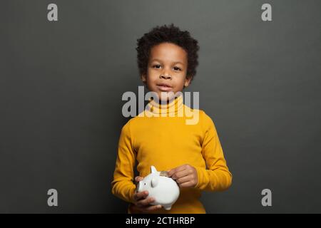 Small black child holding money box and coin on blackboard background Stock Photo