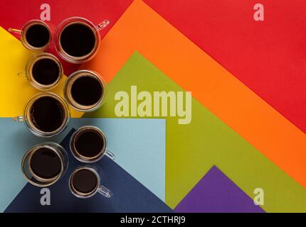 Eight glass round cups with fresh black espresso and Americano coffee. Cups grouped on colorful abstract background with geometric pattern in rainbow Stock Photo