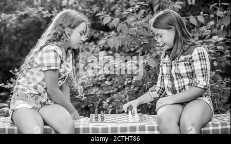 Think better. Children play chess outdoors nature background. Sport and hobby concept. Little girls play chess. Sisters playing chess. Smart children. Early childhood development. Intellectual game. Stock Photo