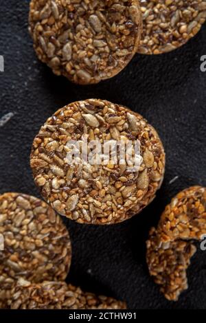 Caramel peanut brittle from sunflower seeds and sesame seeds and fitness cookies with flax seeds on dark black concrete background. Stock Photo