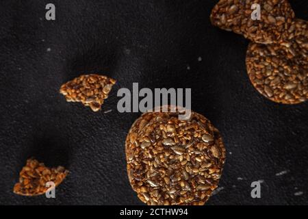 Caramel peanut brittle from sunflower seeds and sesame seeds and fitness cookies with flax seeds on dark black concrete background. Stock Photo