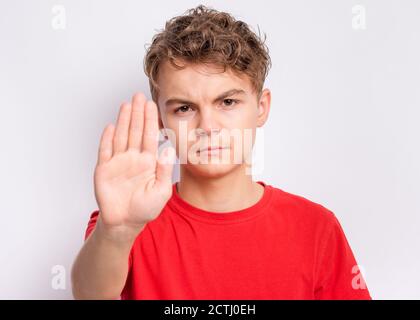 Teen boy doing stop sign with palm of hands, on gray background. Beautiful caucasian teenager making stop gesture. Stock Photo