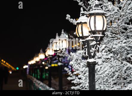 Vintage street lights lit on the streets of the city at night. Winter city landscape. Snow-covered fence and lamps. Stock Photo