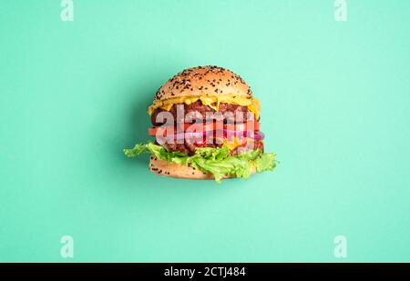 Homemade burger with double beef patties, cheese, and salad isolated on a green-mint background. Single hamburger side-view Stock Photo