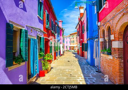 Burano island narrow cobblestone street between colorful houses buildings with multicolored bright walls, blue sky sunny summer day, Venice Province, Veneto Region, Northern Italy. Burano postcard Stock Photo