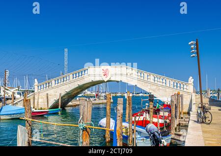 Stone bridge Ponte di Vigo across Vena water canal with colorful boats near pier embankment in historical centre of Chioggia town, blue sky background in summer day, Veneto Region, Northern Italy Stock Photo