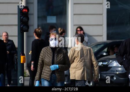 Woman with mask and gloves walking in the city center near red traffic light during Covid or Coronavirus outbreak, masks mandatory, compulsory Stock Photo