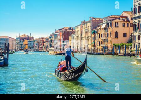 Venice cityscape with Grand Canal waterway, Venetian architecture colorful buildings, gondolier on gondola boat sailing Canal Grande, blue sky in sunny summer day. Veneto Region, Northern Italy. Stock Photo