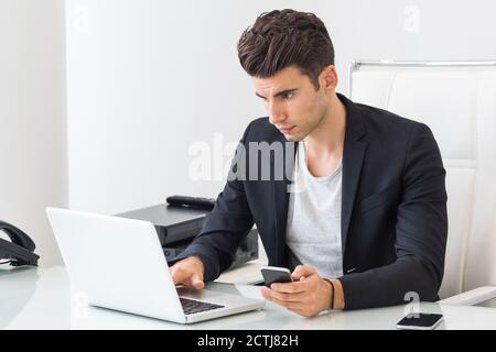 Focused businessman using a laptop computer and mobile phone at work. Stock Photo