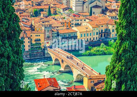 The Ponte Pietra Stone Bridge, Pons Marmoreus, Roman arch bridge across Adige River, buildings with red tiled roofs in Verona historical city centre, cypress trees on the sides, Veneto Region, Italy