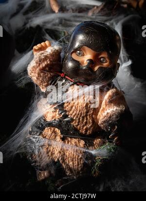 Creepy doll. Halloween decoration. The baby doll is caught in spider webs and is wearing a dark mask. Horror concept. Stock Photo