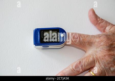 Pulse oximeter on person's finger measuring their oxygen saturation  (SpO2) level and pulse frequency with readout display shown Stock Photo