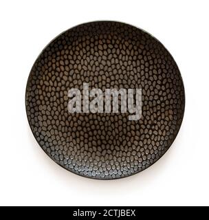 Round black ceramic plate with textured surface isolated on a white background. Empty crockery for food design. Modern clay, ceramics or porcelain. Stock Photo
