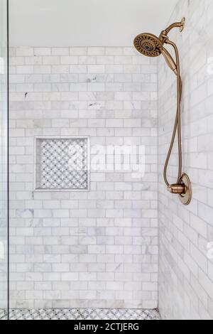 An empty shower with subway tiles and small ceramic tiles on the floor and shelf with a gold shower head. Stock Photo