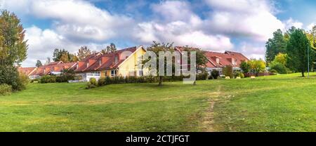 Typical Swedish middle class wooden terraced houses in Umea. Residential yellow townhouses with red orange clay tiles on blue sky with big white cloud Stock Photo