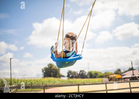 Low angle view of boy swinging outdoors. Stock Photo