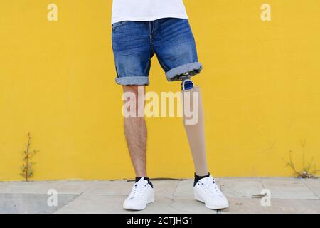 Handicapped male with leg prosthesis in sneakers standing near wall Stock Photo