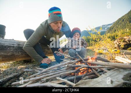 Father and son work together to start a fire at wilderness campsite. Stock Photo