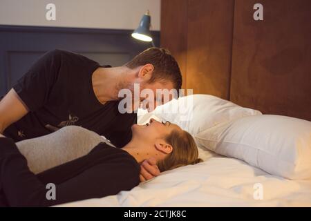 Happy loving couple smiling and looking at each other while lying on bed Stock Photo