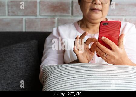 senior woman using mobile phone while sitting on sofa at home Stock Photo