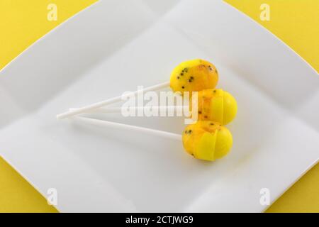 Yellow passionfruit lollipops with bubblegum center on white desert plate on yellow background Stock Photo
