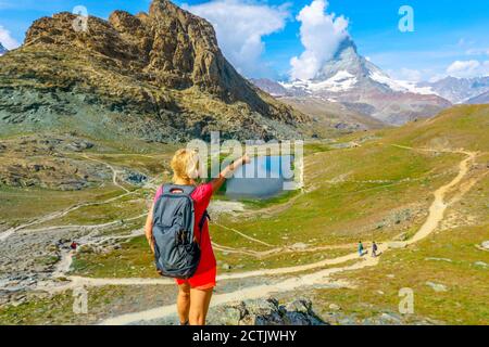 Hiker woman backpacker pointing Mount Matterhorn or Monte Cervino or Mont Cervin, and Swiss Alps and Riffelsee Lake. Activity outdoor in Zermatt Stock Photo