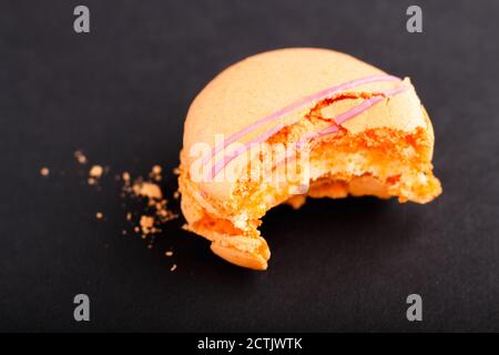 Bitten orange macaron or macaroon cake on black background. side view, close up, macro, selective focus. Stock Photo