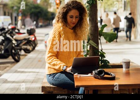 Young female student using digital tablet while sitting at sidewalk cafe in city Stock Photo