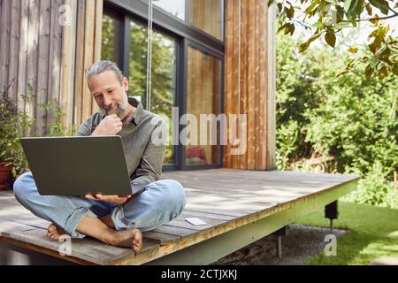 Bearded man using laptop while sitting outside house Stock Photo