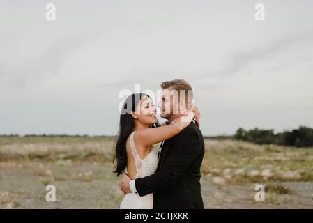 Smiling bride and groom looking at each other in field against sky Stock Photo
