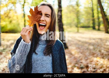 Young laughing woman holding autumn leave on her eye Stock Photo