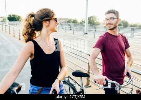 Couple talking while walking with bicycles on bridge against clear sky Stock Photo