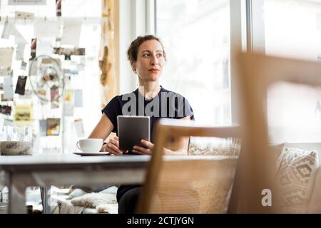 Thoughtful female owner with coffee on table using digital tablet in restaurant Stock Photo