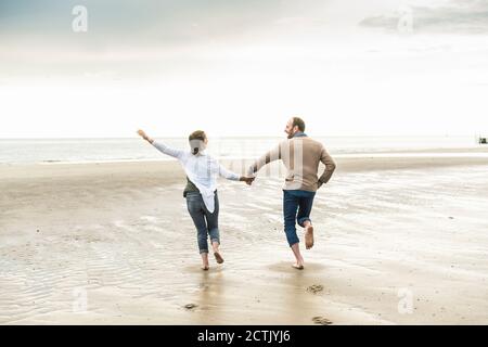 Cheerful couple holding hands while running at beach during sunset Stock Photo