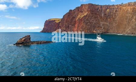 An aerial view of a charter fishing boat cruising along the cliffs and Sharkfin Rock on the Southwest side of the island of Lanai, Hawaii, USA. Stock Photo