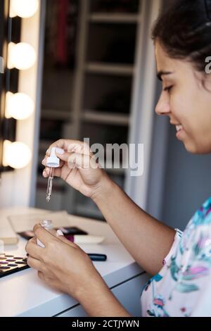 Young woman looking at cosmetic serum while sitting at home Stock Photo