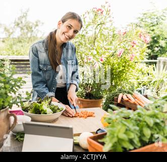 Smiling woman chopping vegetables on cutting board in yard Stock Photo